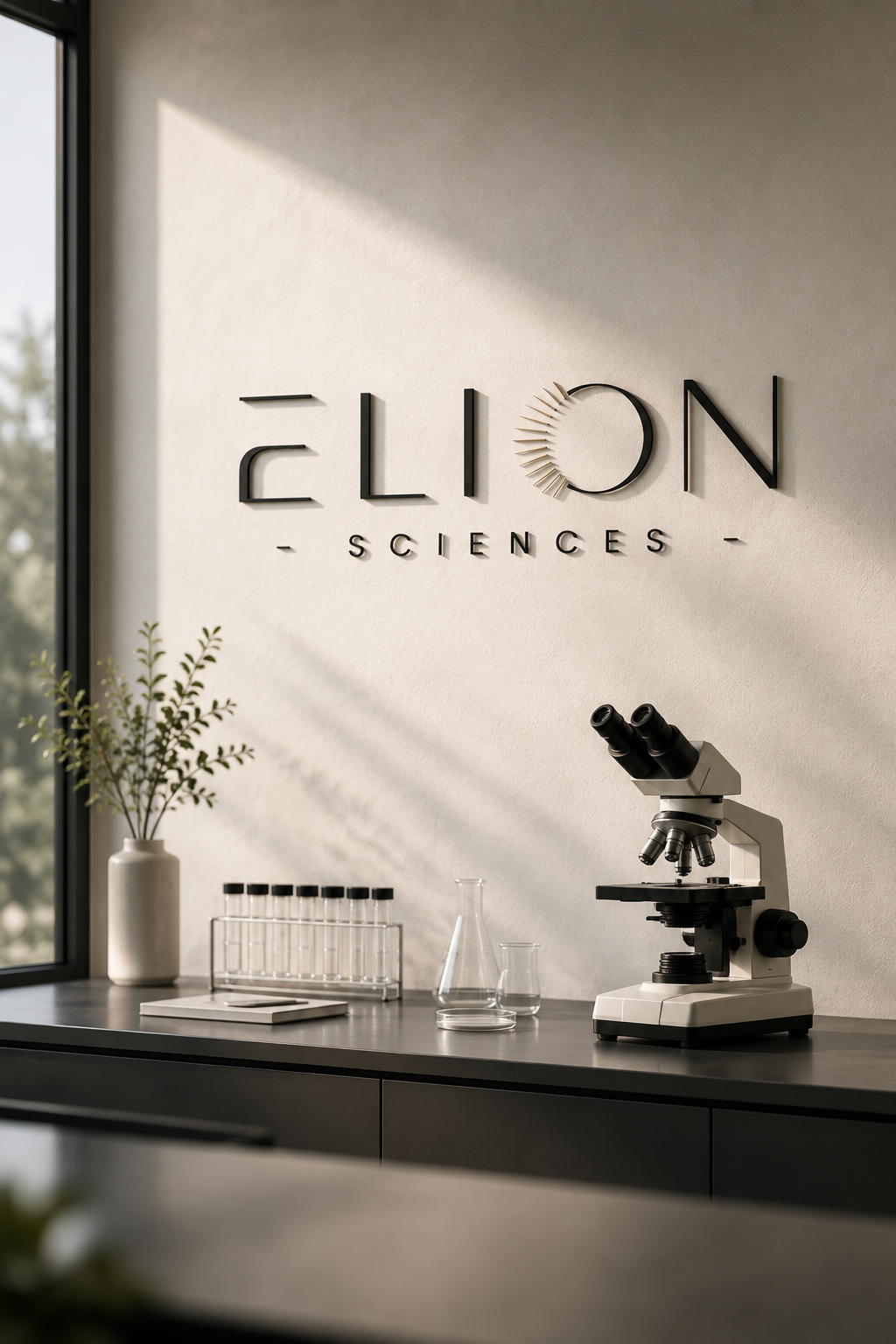 Modern Elion Sciences research laboratory with the Elion logo mounted on a softly lit wall above a clean workbench featuring a microscope, laboratory glassware, and test tubes.